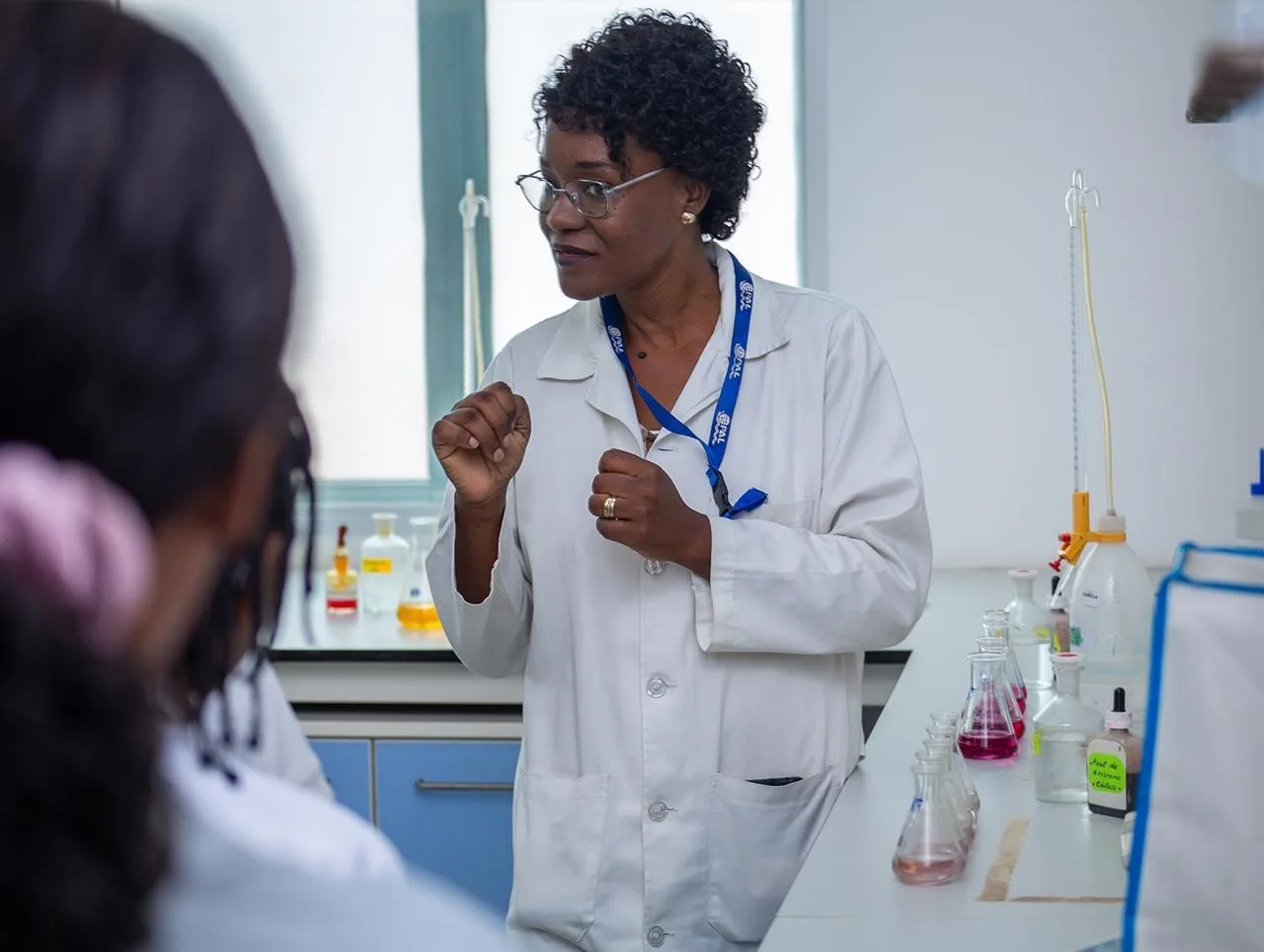 Professora do Colégio Cultus em bata branca durante aula prática em laboratório